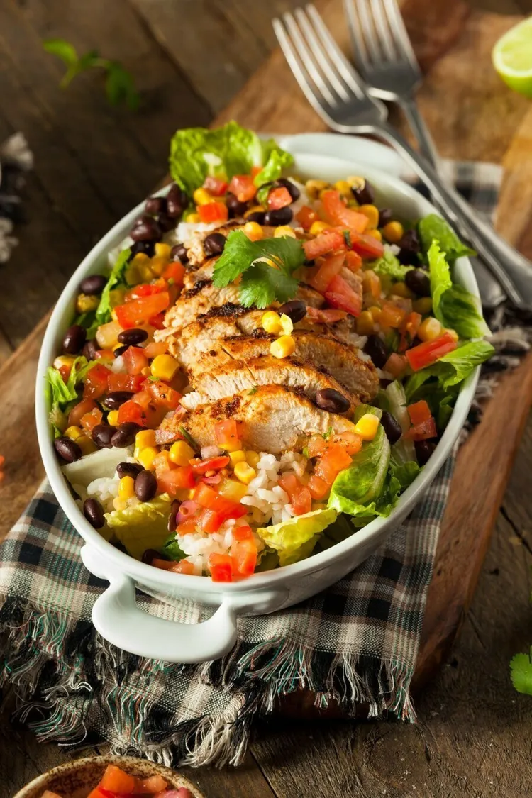 Chicken burrito bowl with avocado, lettuce, green pepper, tomatoes, sweet corn and black beans
